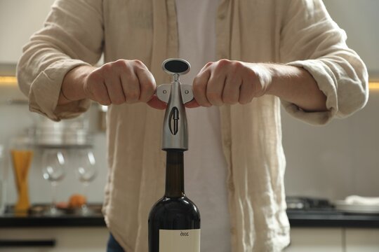 Man opening wine bottle with corkscrew in kitchen, closeup - Powered by Adobe
