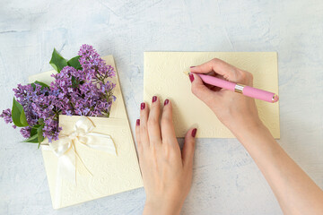 Flat lay with spring blossom. spring or summer concept. woman's hands writing on empty card or blank near purple flowers in a beautiful envelope with a bow. Beautiful lilac flowers. copy space