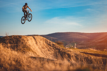 Young man on a mountain bike performing a dirt jump - obrazy, fototapety, plakaty