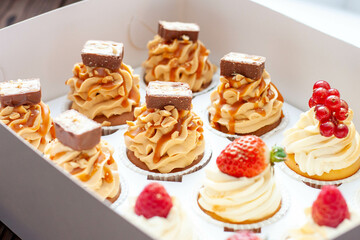 Set of different delicious cupcakes with fresh berries in a paper box on wooden background, horizontal