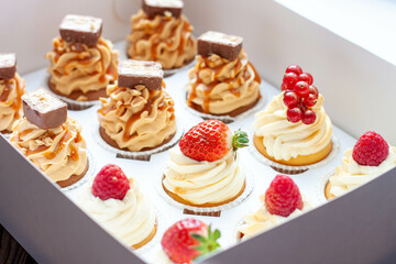 Set of different delicious cupcakes with fresh berries in a paper box on wooden background, horizontal