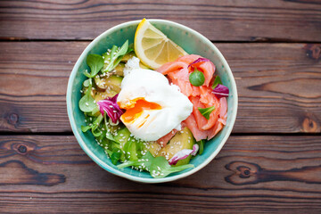 Brunch with poached egg, avocado, arugula, flax seeds and salted salmon on a rustic wooden background. flatlay, horizontal. copy space