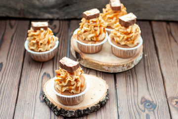 Delicious chocolate cupcakes with peanut butter frosting, chocolate bites and salted caramel sauce on rustic wooden background
