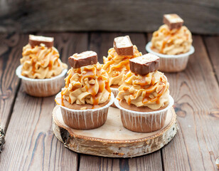Delicious chocolate cupcakes with peanut butter frosting, chocolate bites and salted caramel sauce on rustic wooden background