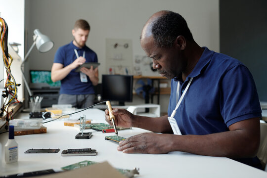 Experienced African American engineer of repair service office sitting by workplace in coworking space and checking computer motherboard - Powered by Adobe