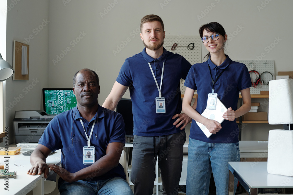 Poster group of intercultural professional technicians in blue uniform looking at camera while standing by 