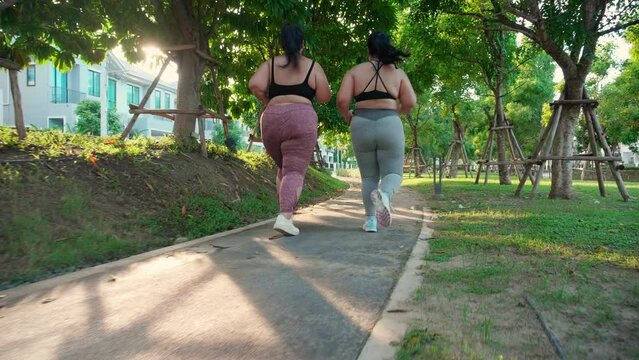 Two asian woman fat in sportswear jogging together on pathway at park, woman and friends obesity doing activity with cardio or running, workout and exercise, plus size and health for weightloss.