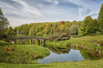 The lake and Palladian arched bridge with the pantheon temple in the distance at Stourhead Park and...