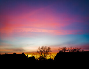 Colorful sky during sunset over silhouettes of houses and trees.