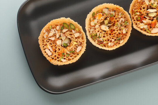 Rajasthani Ghevar. Ghewar is an Indian crunchy sweet dish made using refined flour, sugar, and ghee. Garnished with silver foil and dry fruits.