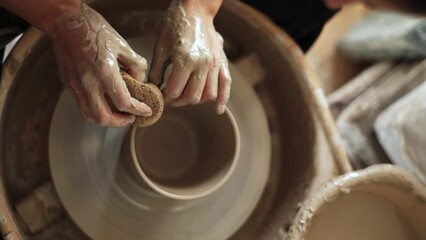 Overhead shot capturing a potter's hands gently smoothing the surface of a clay piece on the wheel using a wet sponge