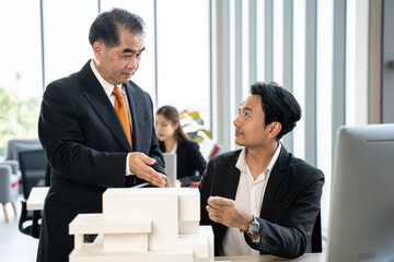 Fototapeta na wymiar Young asian man presents a building model to boss at the office. They discuss building design together in the office.