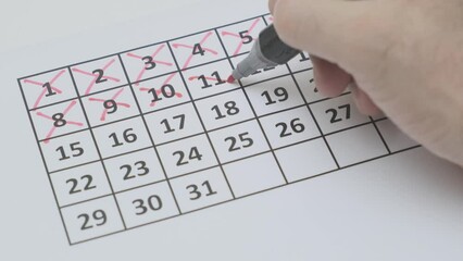 crossing out days of number in calendar grid with red marker, close-up, slow motion, selective focus
