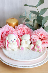 Cute edible teddy bear and bunny toys made of white chocolate with fresh peonies and candles on the backgrounds. Gift for a baby