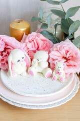 Cute edible teddy bear and bunny toys made of white chocolate with fresh peonies and candles on the backgrounds. Gift for a baby