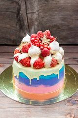 Pink, violet and blue cake with melted white chocolate, fresh strawberries dipped into chocolate, raspberries, red currant and meringues