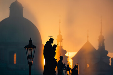 Statues on Charles Bridge against urban skyline with church and towers.  Beautiful sunrise in Prague, Czech Republic.. - obrazy, fototapety, plakaty