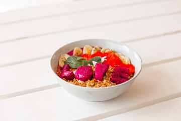 Nut muesli with fruits, berries and love. Delicious smoothie bowl with granola and dragonfruit on a white wooden table. The concept of a delicious and healthy breakfast