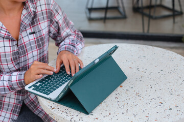 The woman works and studies online. Concept of freelancing and working remotely with space for text. Blogger typing on tab computer in cafe