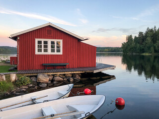Rotes Holzhaus am See und Steg mit zwei weißen Ruderbooten vor dem Blick über den See beim...