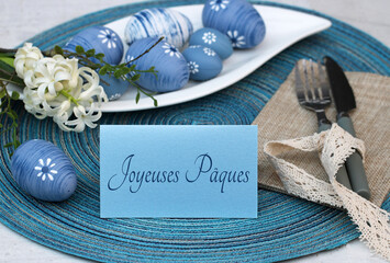 Placez la carte avec le texte Joyeuses Pâques sur une assiette avec des couverts et des fleurs.