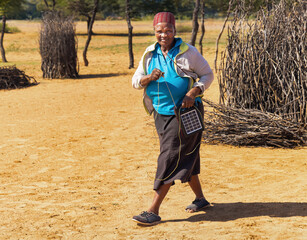 village old african woman using a solar panel with radio, to recharge phones and light, donated by...