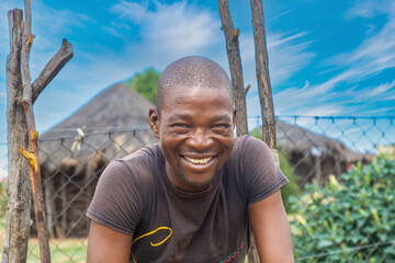 village happy african men, with a toothy smile, standing in front of a thatched hut.