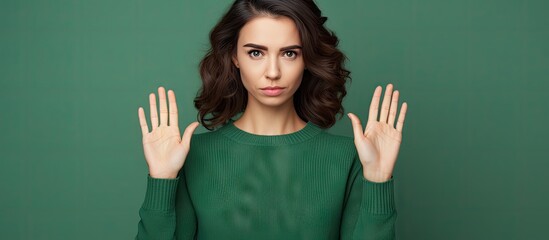 Young woman expressing frustration with tiny size gesture, hands spread up in the air on green background - obrazy, fototapety, plakaty