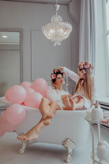Mom and daughter in pink pajamas and curlers having fun in bathroom
