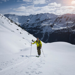 Man on mountain ski tour in the snow on sunny day, winter mountain panorama in background. - 745922336