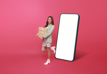 Happy Asian woman smiling and holding package parcel box with mockup big smartphone blank white...