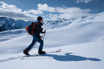 Man on mountain ski tour in the snow on sunny day, winter mountain panorama in background. - 745922584