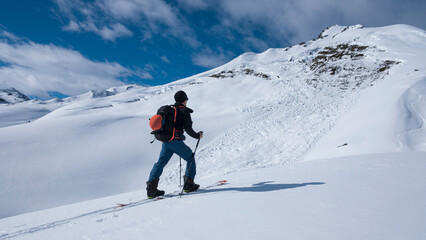 Fototapeta na wymiar Man on mountain ski tour in the snow on sunny day, looking at avalanche.