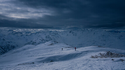 Two people on mountain ski tour during dramatic dark weather conditions, dark clouds in the sky. - 745922737