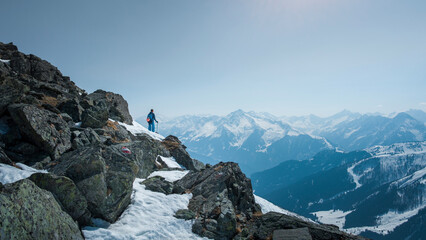 Man in between mountain rocks in winter, looking at mountain panorama on a sunny day. - 745922939