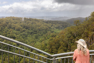 A woman, on a round-the-world adventure tour, stands on the Minyon Falls lookout in Nightcap National Park near Alstonville, NSW, Australia. The park is home to a World Heritage-listed rain forest.