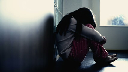 Sad child suffering from depression sitting alone in corridor feeling loneliness. Scared fearful...