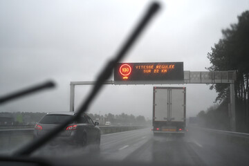 car driving in the rain with sign indicating regulated speed for 22 km