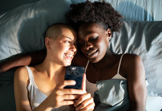 Lesbian couple looking at smartphone in bed together