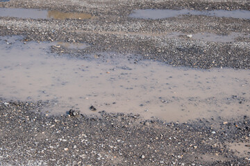 Puddle on old, muddy and damaged asphalt floor. Very bad quality road.