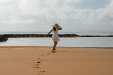 Woman on the beach with hat walking and white dress dancing