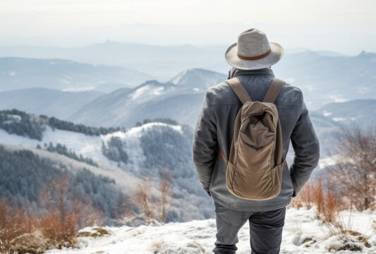 Back view of a hiker with backpack and hat standing on a snow mountain