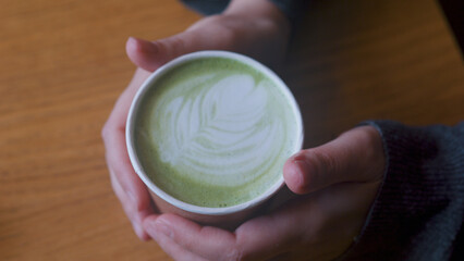 Female hands holding paper cup with green matcha latte. Close up.