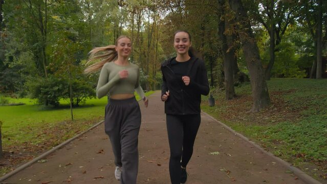 Happy women active fit sporty girls Caucasian ladies jogging running together in park outdoors two happy smiling sportswomen female joggers runners healthy lifestyle morning jog run in city outside