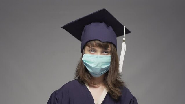 Graduation girl putting on cap. Female student wearing protective face mask. Unsuccessful try.