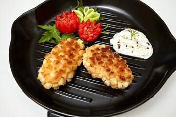 Fried minced meat cutlets with vegetables and sauce on black pan close-up. Chicken Pozharsky cutlets. Isolated on white background.