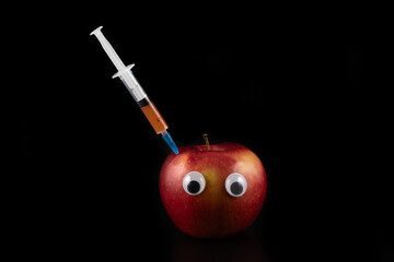 Syringe and red apple with eyes on a black background