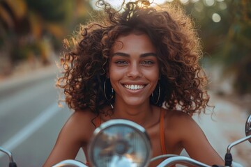 Fototapeta premium Radiant young woman with curly hair enjoying a scooter ride at sunset, tropical setting