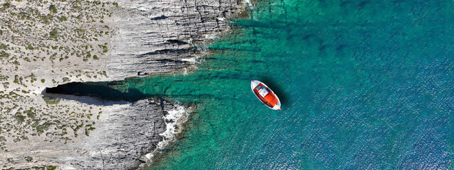 Aerial drone top down ultra wide photo of red traditional wooden fishing boat anchored in volcanic...