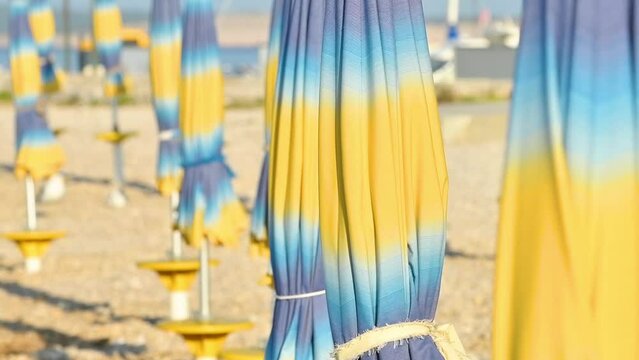 Folded colorful beach umbrella parasols on Adriatic sea coast in sunny summer morning, holiday and vacation background